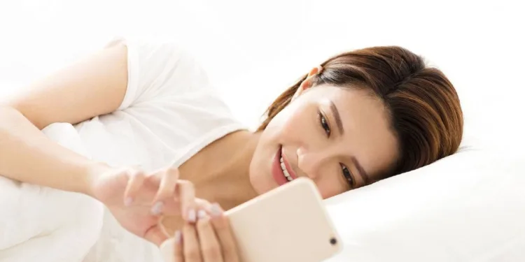 Young woman indulging in social media on smartphone while lying in bed — symbolizing digital overuse.