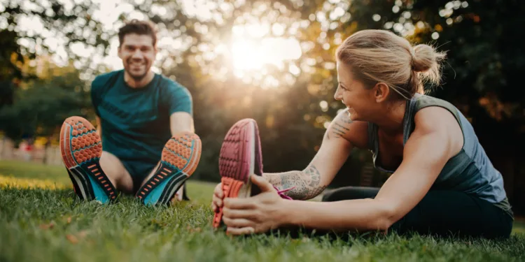 Man and woman stretching together in a park during sunset, promoting physical and mental well-being.