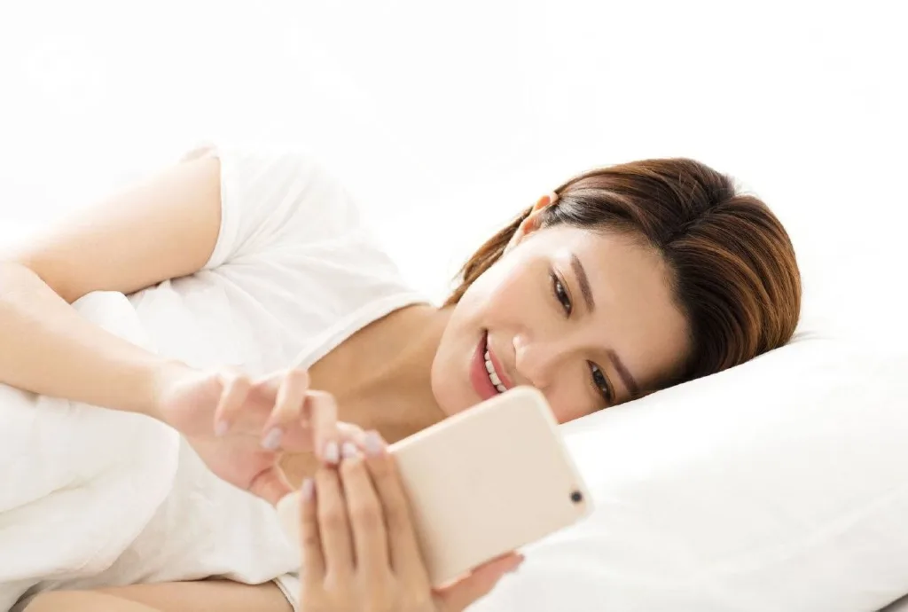Young woman indulging in social media on smartphone while lying in bed — symbolizing digital overuse.