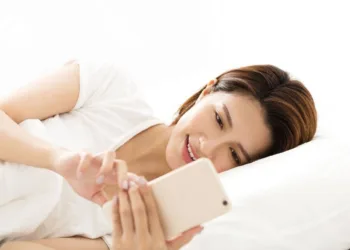 Young woman indulging in social media on smartphone while lying in bed — symbolizing digital overuse.